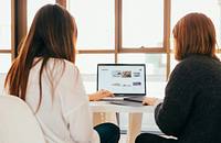Two women facing a laptop centered between them, with an ecommerce site on the screen.