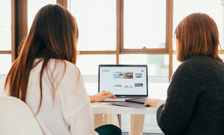 Two women facing a laptop centered between them, with an ecommerce site on the screen.