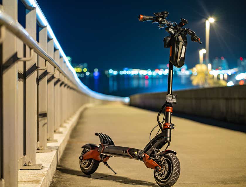 A red and black electric scooter parked on a bridge.