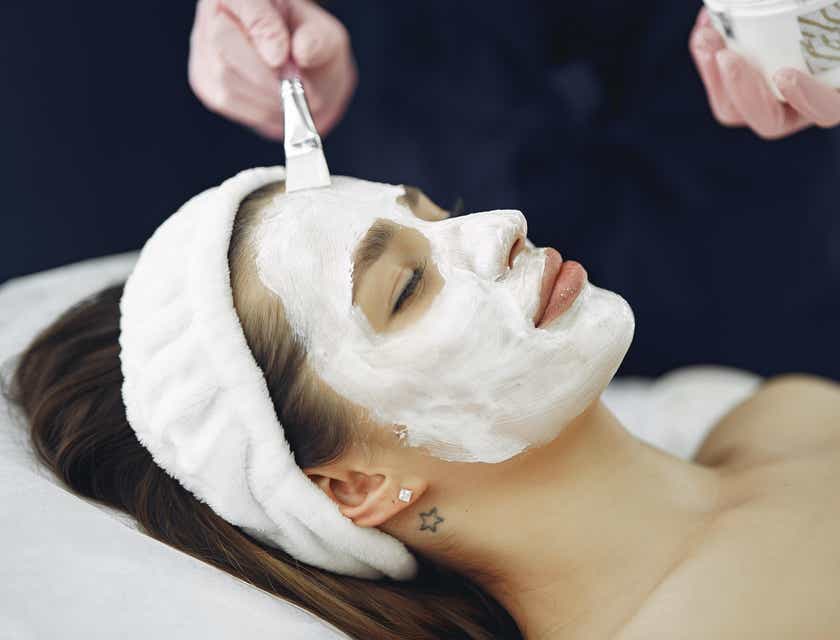 Eine Frau lässt sich in einem Schönheitssalon eine weiße Gesichtsmaske auftragen.