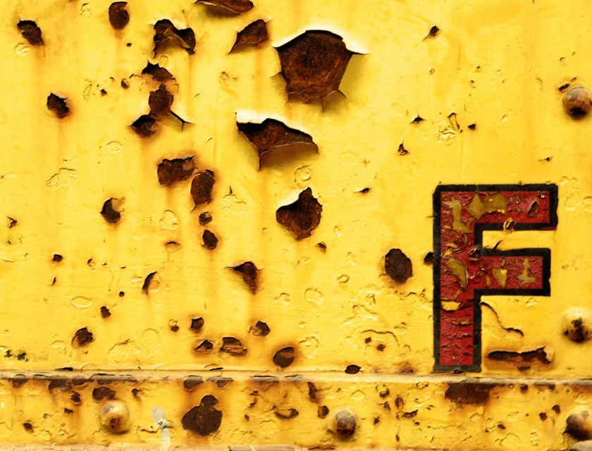 Une lettrine F rouillée affichée sur un mur jaune écaillé.