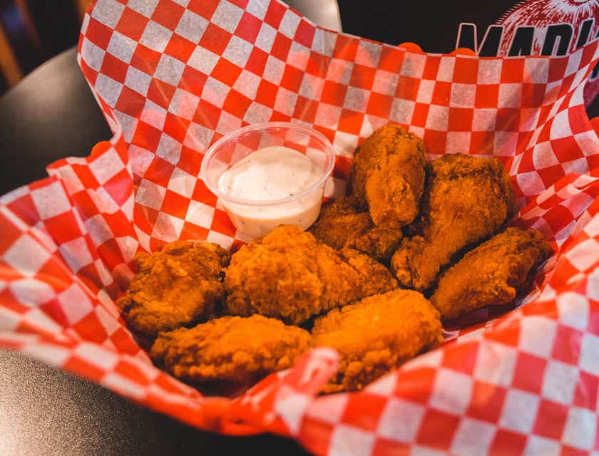 A basket of fried chicken with a side of ranch is displayed on a white and red napkin.