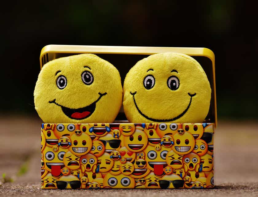 Śmieszne, żółte pluszaki w kształcie emotikonek wystające z metalowego pudełka.