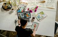 A graphic designer working on a project at a laptop and tablet.