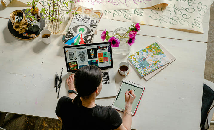 A graphic designer working on a project at a laptop and tablet.
