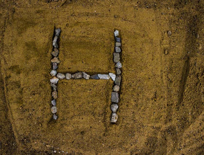 La lettre H composée de galets posés dans du sable.