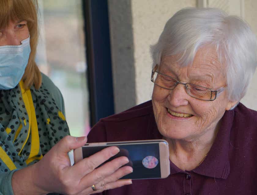 Een huiszorgverpleegster houdt een mobiele telefoon omhoog zodat een oudere vrouw het scherm kan zien.