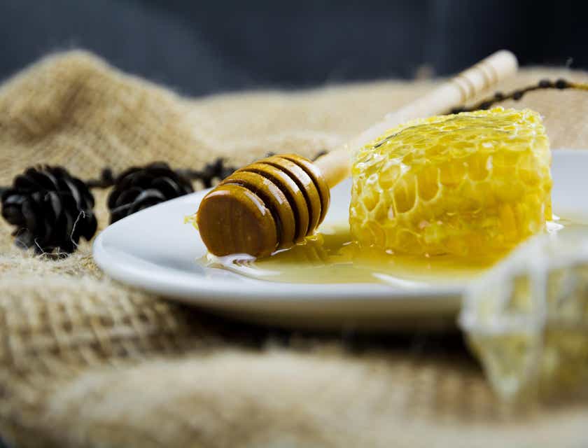 Uma concha de mel do lado de um favo de mel em um prato branco.
