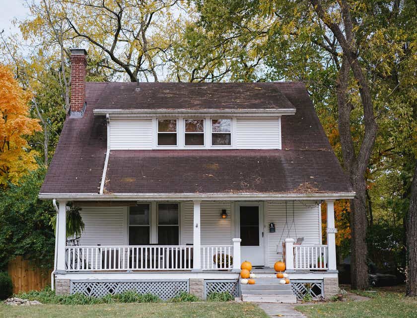 Una casa blanca con un porche rodeada de árboles, en un logo de casa.