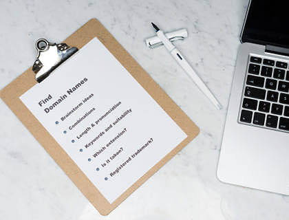 A clipboard next to a laptop with a page titled "Find Domain Names."