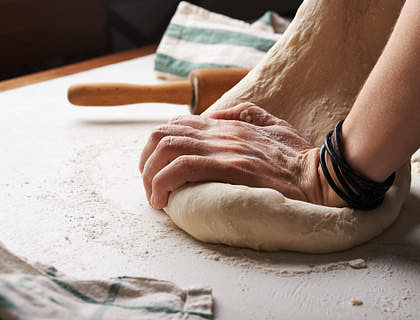 Person kneading dough on a flour-covered surface in a bakery.