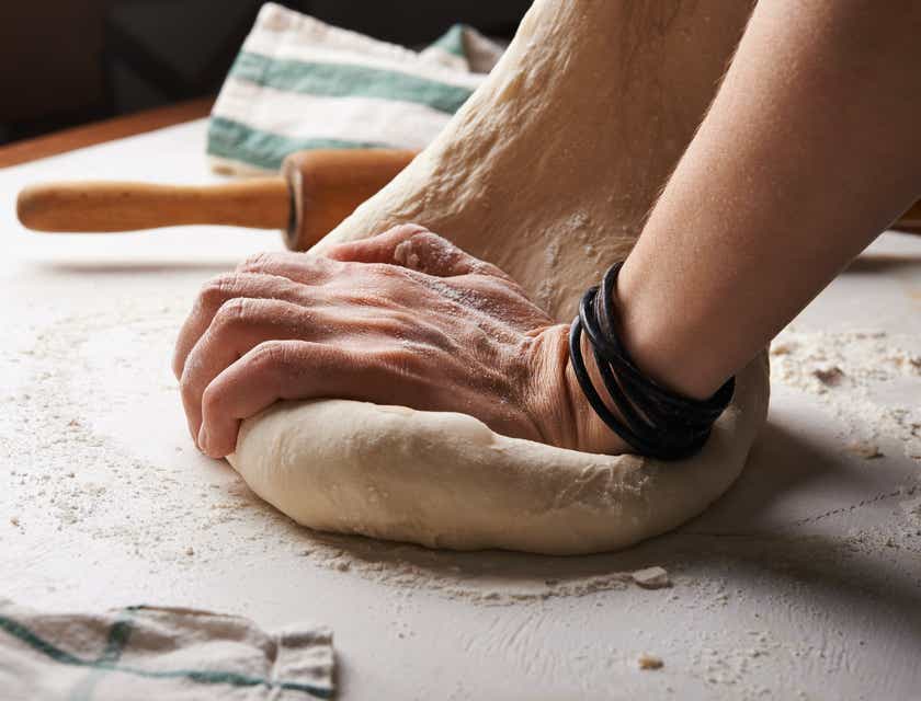 Seseorang sedang menguleni adonan yang dilapisi tepung di suatu bakery.