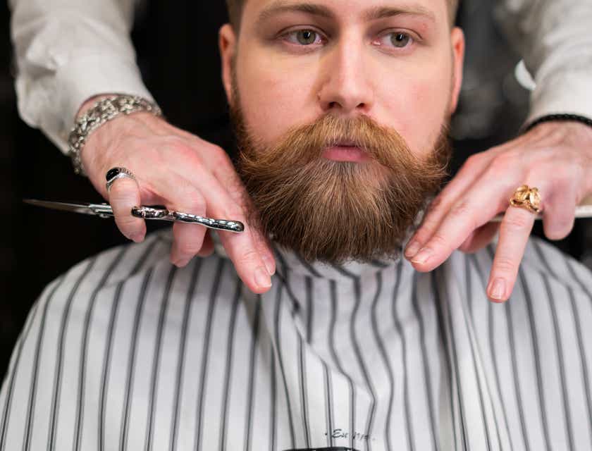 Seorang barber sedang mencukur janggut pelanggan di sebuah barbershop.