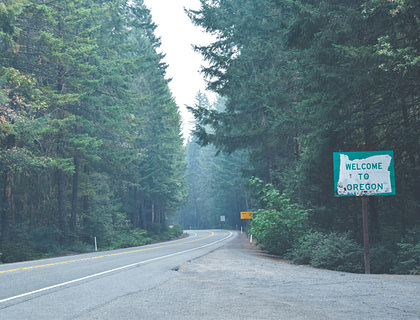 Road passing through a forest with a sign next to it that says welcome to Oregon.