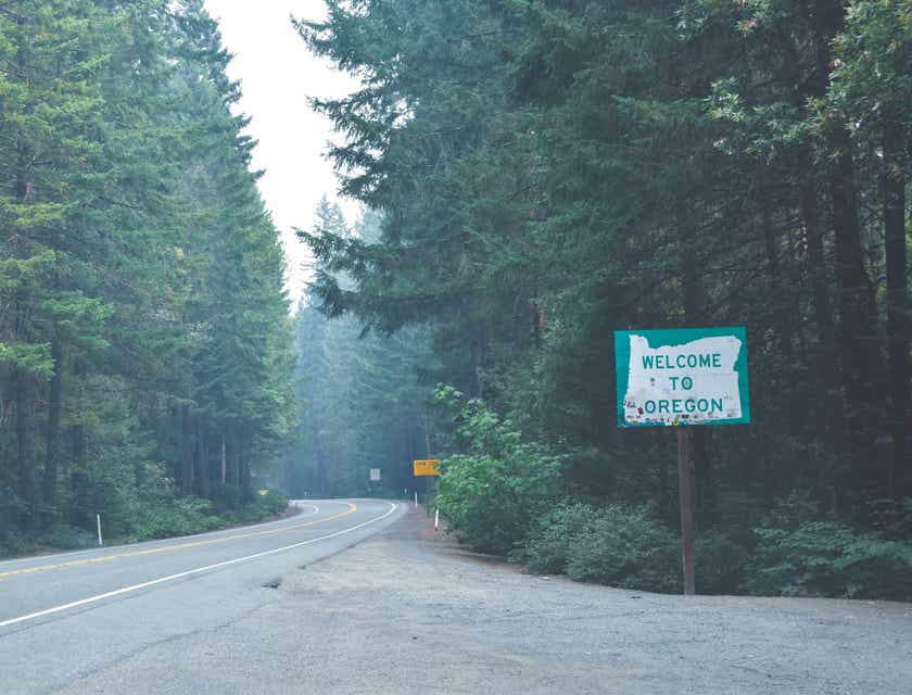 Road passing through a forest with a sign next to it that says welcome to Oregon.