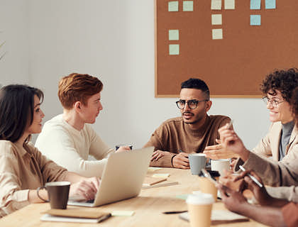 People sitting around a light brown table having a meeting.