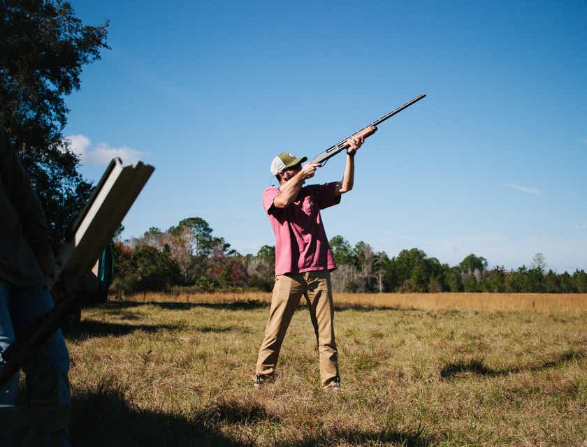 Un homme en train de viser avec un fusil de chasse dans un champ ouvert.
