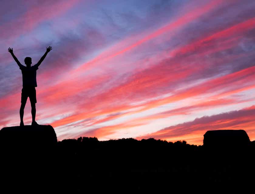 An inspirational person standing at the top of a mountain at sunset.