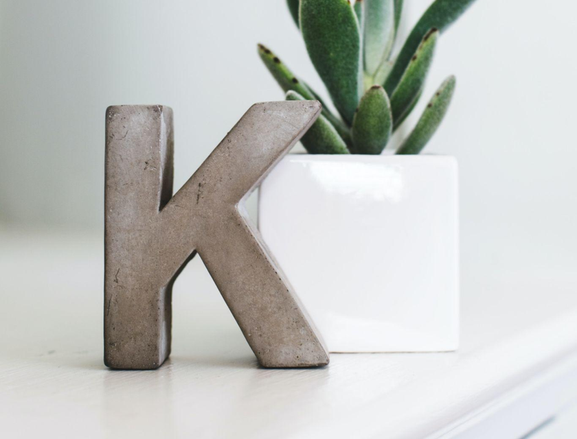Un soprammobile a forma di lettera "K" messo su un tavolo bianco accanto a una piantina in un vaso.