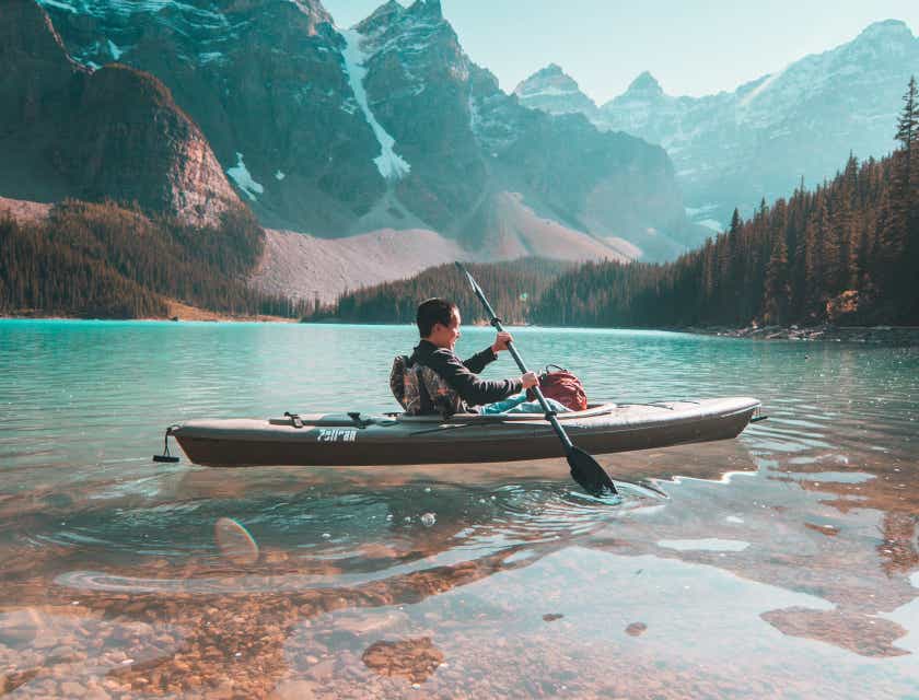 Seseorang di danau mengendarai kayak dengan pegunungan di _background_.