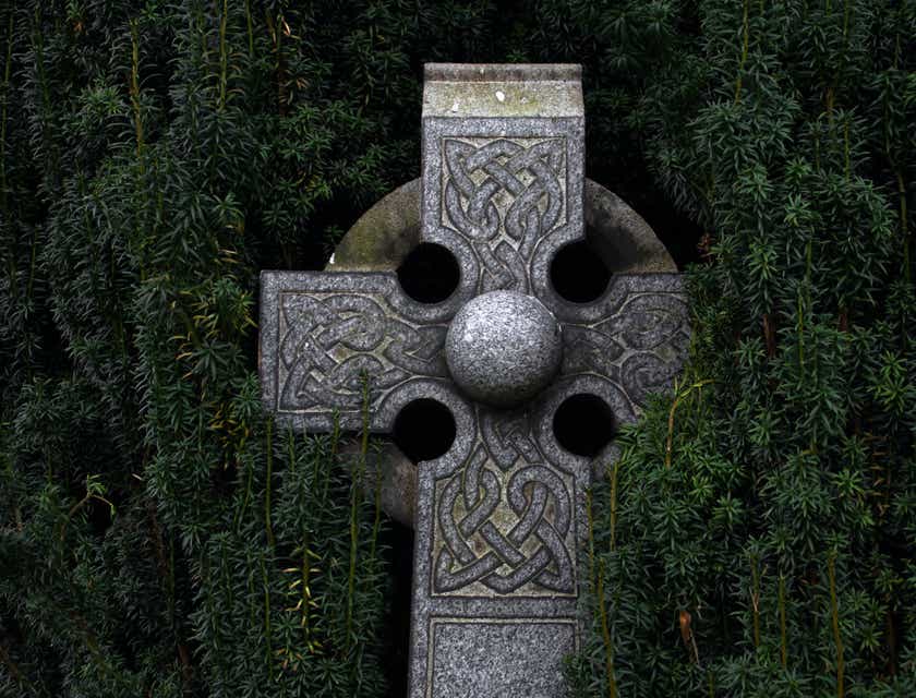 Een rijk versierd Keltisch kruis met een groene heg als achtergrond.