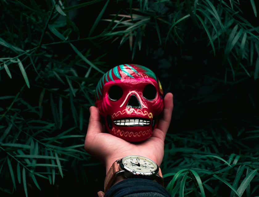A hand holding a colorfully painted skull sculpture.