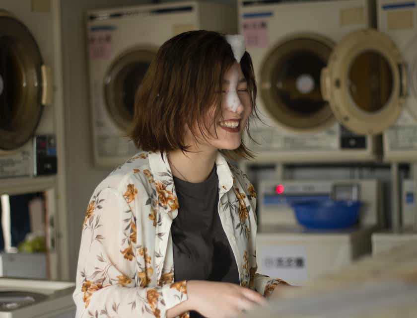 Una mujer tiene algunas burbujas en la cara mientras lava su ropa dentro de una lavandería automática.