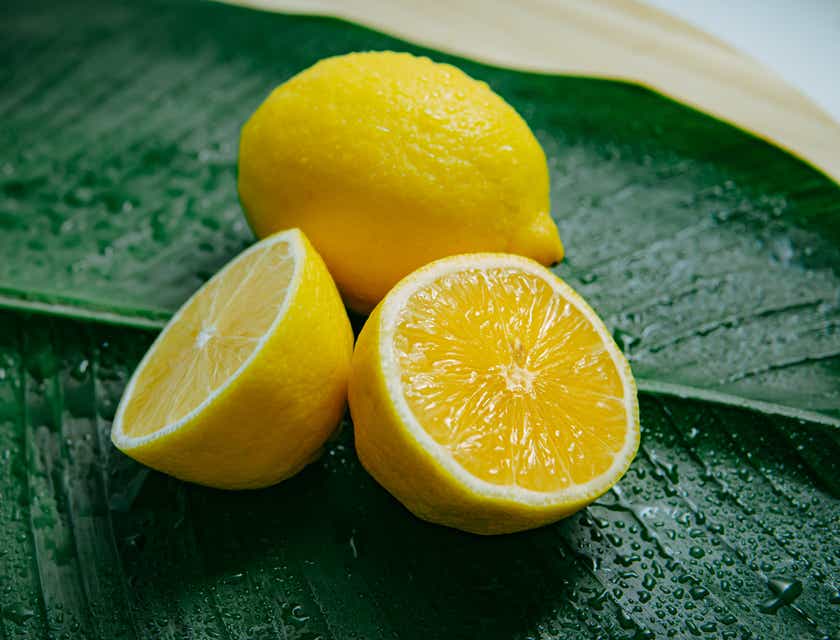 Yeşil bir yaprağın üzerinde bir tanesi yarıya bölünmüş iki limon.