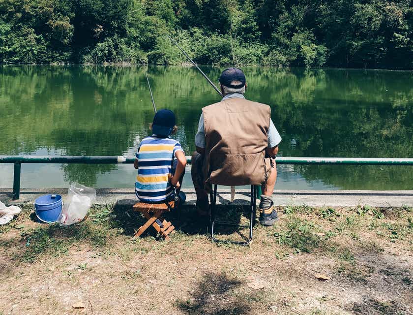 Seorang kakek dan cucu sedang mancing di pinggir danau.