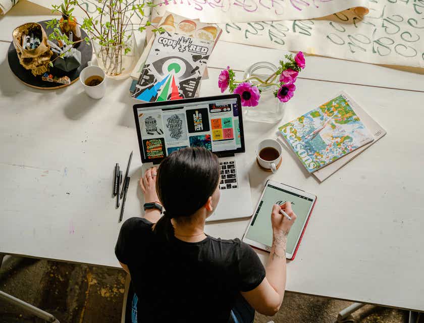 Eine Grafikdesignerin sitzt vor einem Laptop und Tablet und arbeitet an neuen Designtrends.