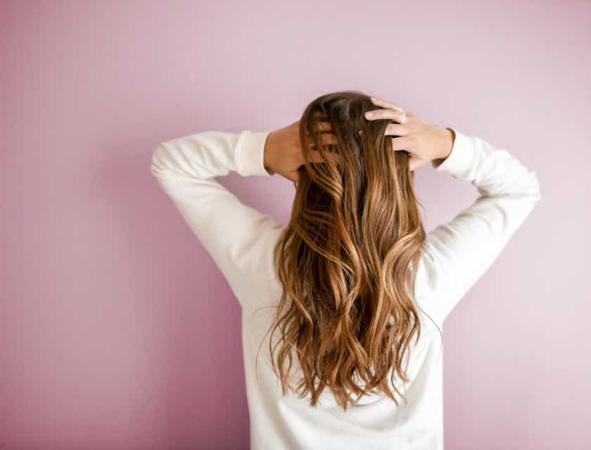 Una mujer parada de espaldas peinando su cabello con las manos.