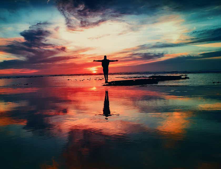 Une personne spirituelle avec les bras tendus pendant un coucher de soleil sur la plage.