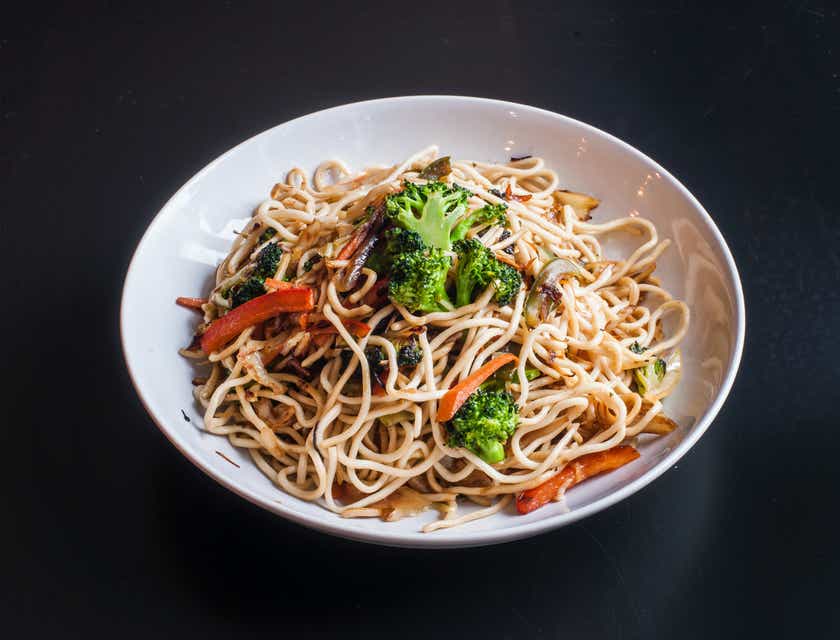 Un plato hondo lleno de fideos con diferentes verduras sobre una mesa de color negro en un restaurante de fideos.