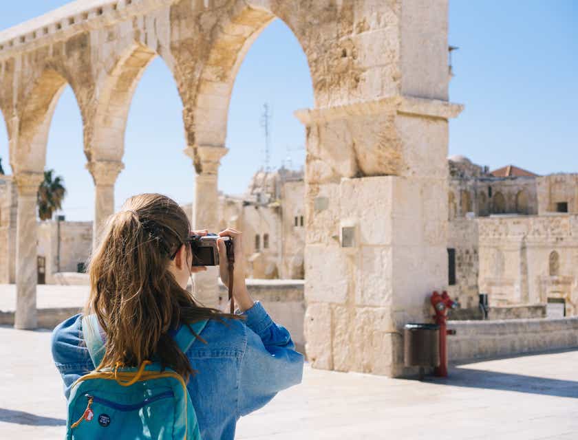 Una mujer tomando fotos en un lugar turístico que incluye ruinas antiguas, en un logo para turismo.