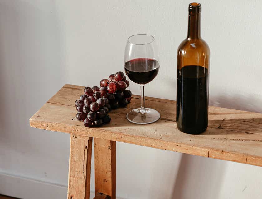 Una botella de vino, una copa y un racimo de uvas sobre una mesa de madera.