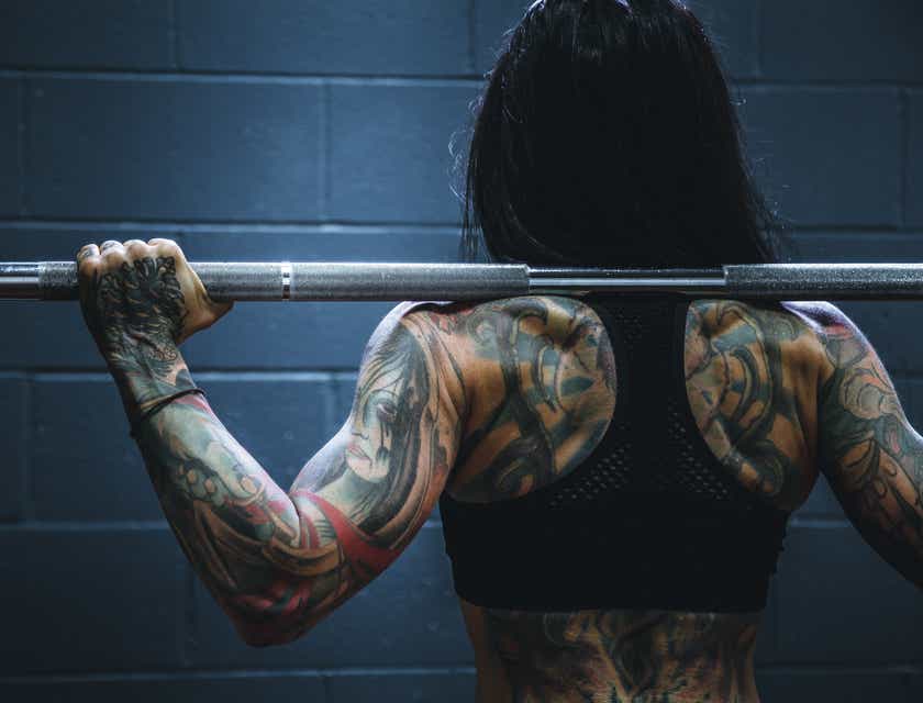 Una mujer ruda con tatuajes sosteniendo una barra en un logo rudo.