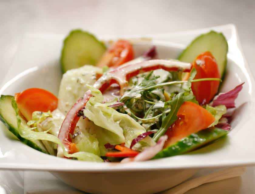 Uma salada preparada na hora servida em uma tigela branca rasa.