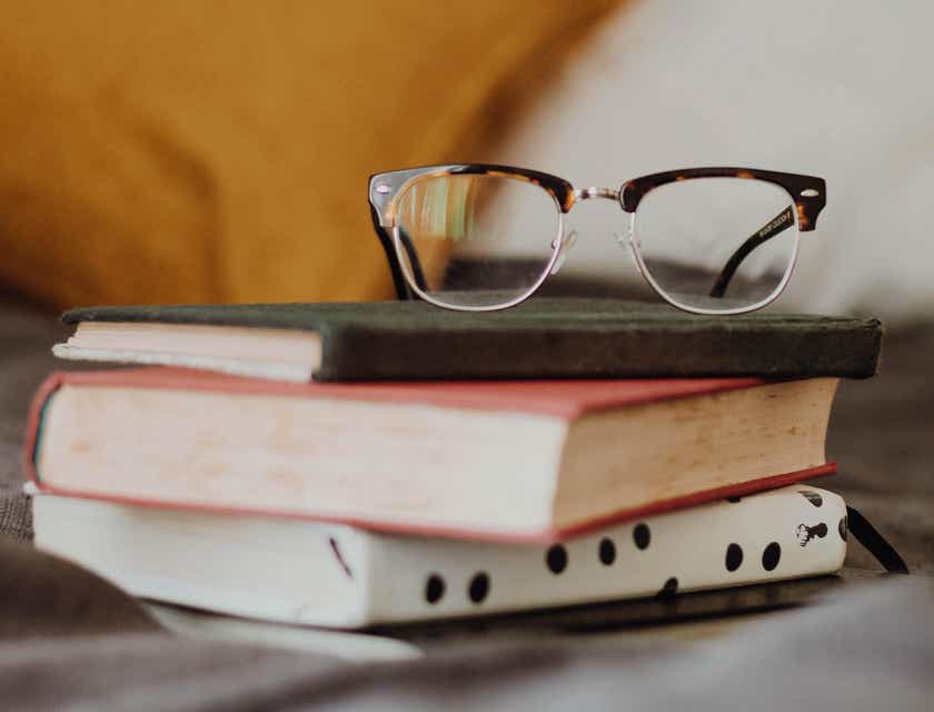 Eine streberisch wirkende Brille liegt auf einem Stapel Bücher.