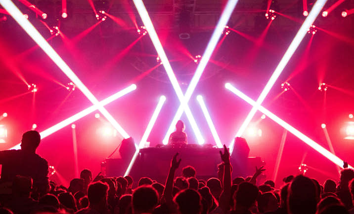 A crowd of people dancing in front of a DJ in a nightclub with laser lights.