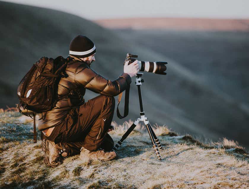 Un photographe accroupi au sommet d'une montagne prend des photos pour son entreprise de photographie.