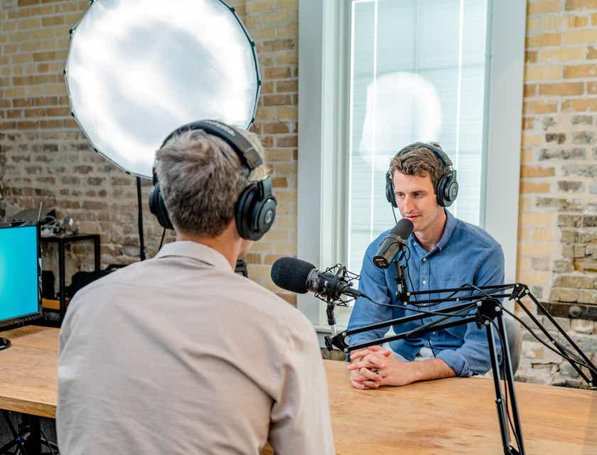 Dos hombres hablando frente a sus micrófonos grabando un podcast en un estudio.