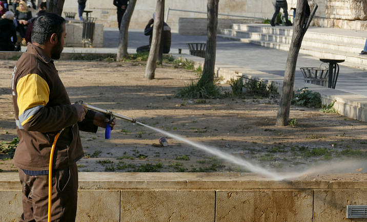 A man in a brown utility uniform pressure washing a city wall.