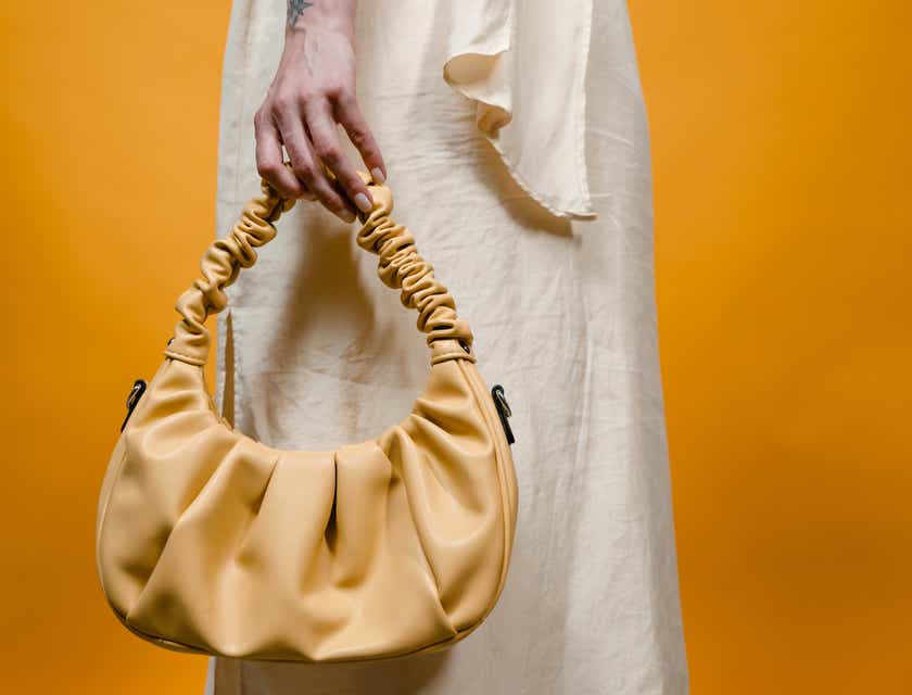 A brown purse held by a person in a cream dress.