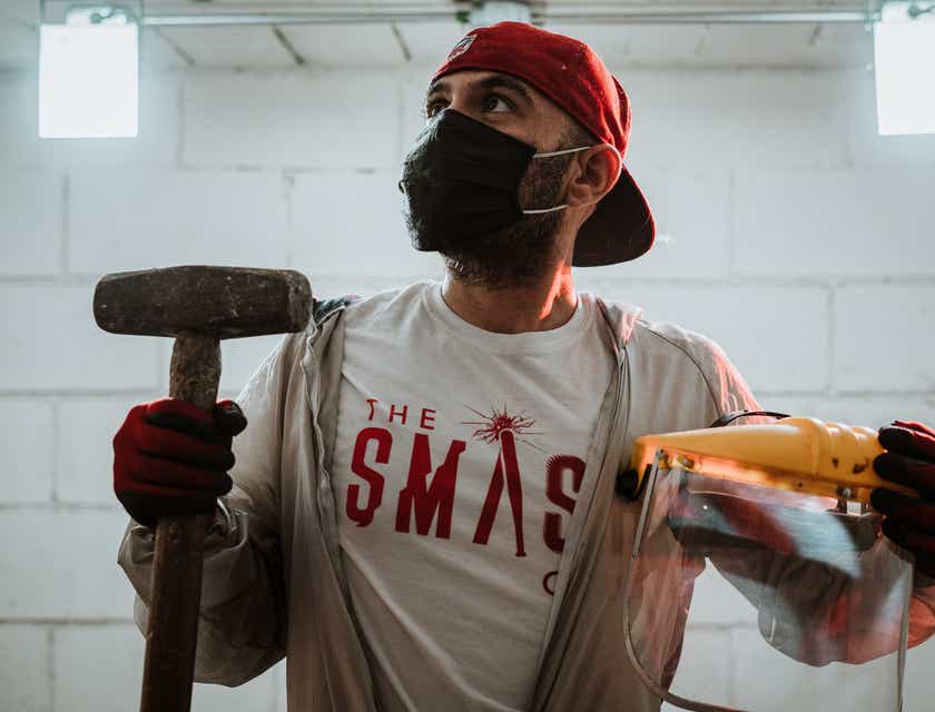 A man holding a sledge hammer and protective gear at a rage room business.