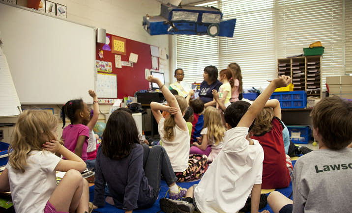 Children sitting on the floor in a classroom at school, having a conversation.