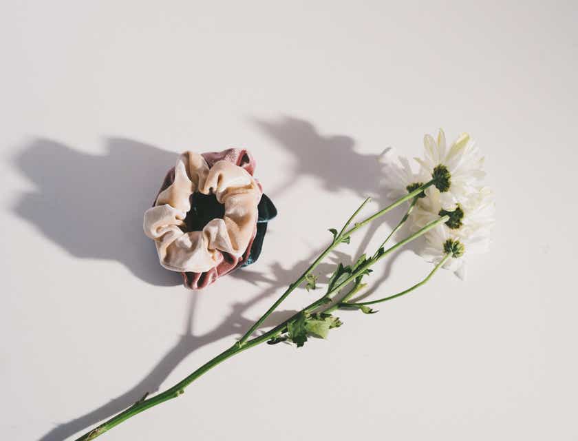 Scrunchie di sebuah permukaan putih dengan bunga di sebelahnya.