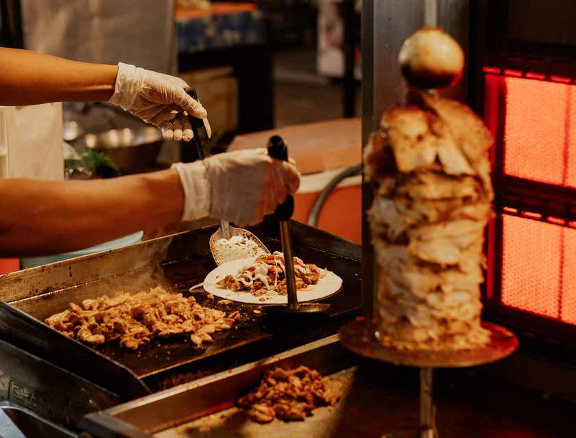 A man plating a shawarma with lots of meat sliced from the spit.