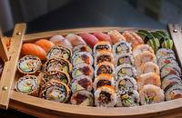 A boat-shaped wooden serving dish filled with various styles of sushi.