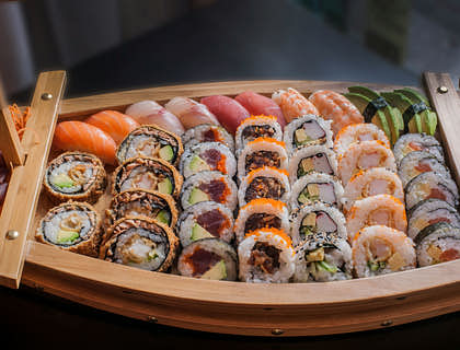 A boat-shaped wooden serving dish filled with various styles of sushi.