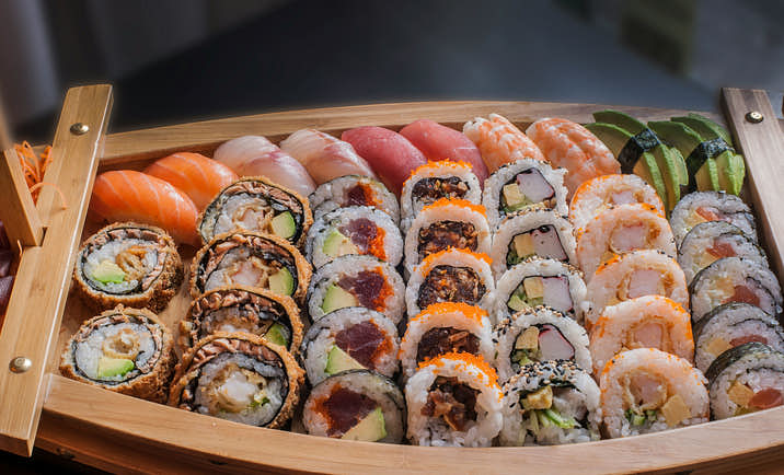 A boat-shaped wooden serving dish filled with various styles of sushi.